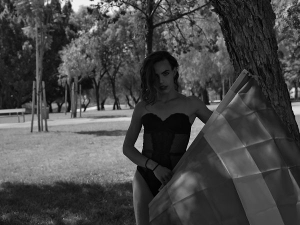 Young Hispanic and transgender adult girl in her underwear, holding a gay pride flag outdoors. Concept of transsexuality, inclusion and diversity.